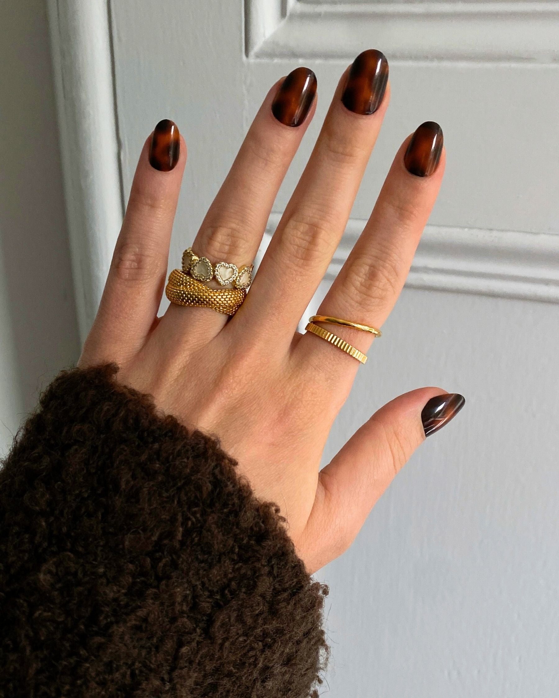 Hand with gold rings and Loste press-on nails in a tortoiseshell design