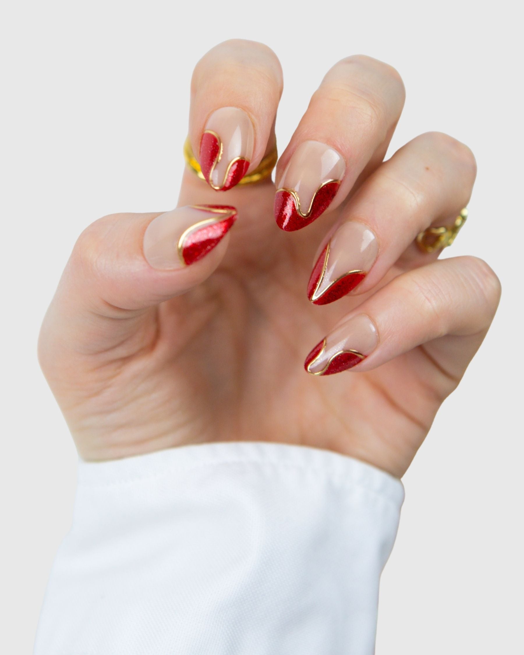 A hand wearing Loste false nails featuring red French nails with a gold and glitter design 