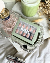 A flat lay with matcha, perfume and flowers and a box of Loste press-on nails in a black and white polka dot design in the middle of the image