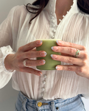 Two hands holding a cup of matcha wearing Loste press-on nails in a black and white polka-dot design