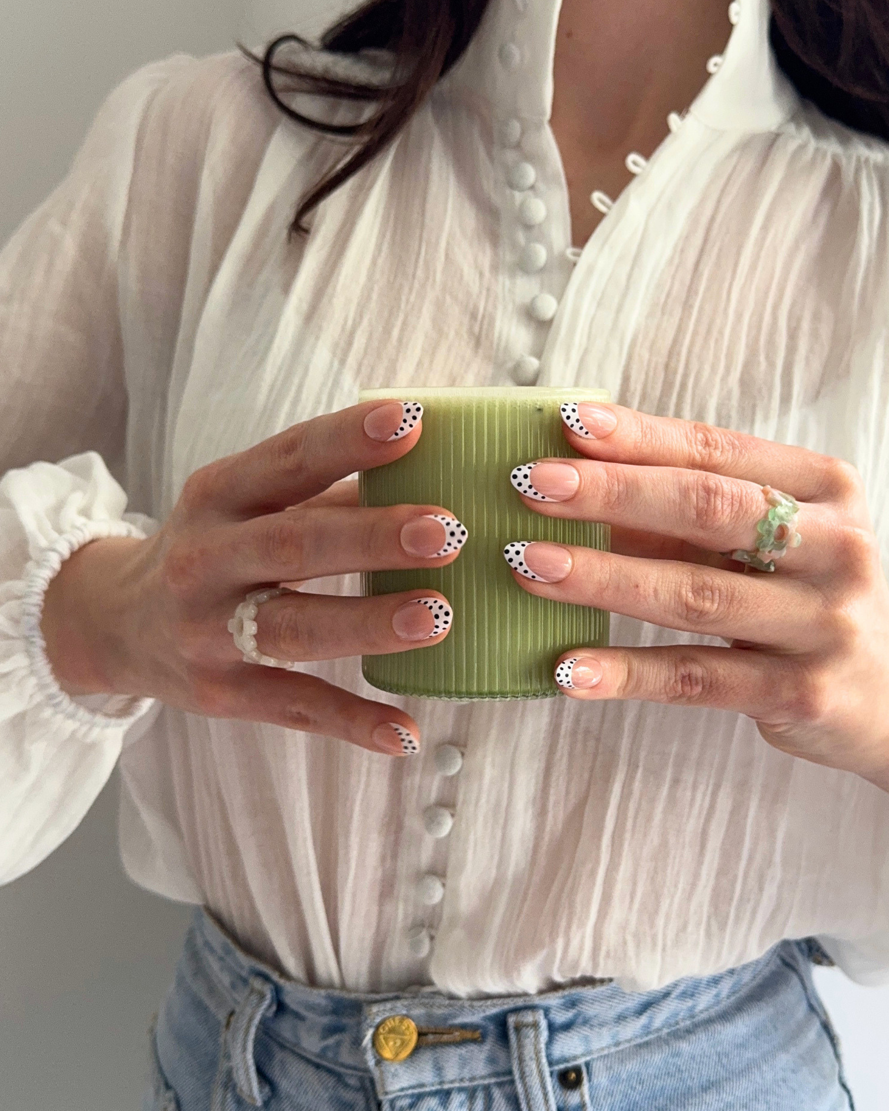 Two hands holding a cup of matcha wearing Loste press-on nails in a black and white polka-dot design