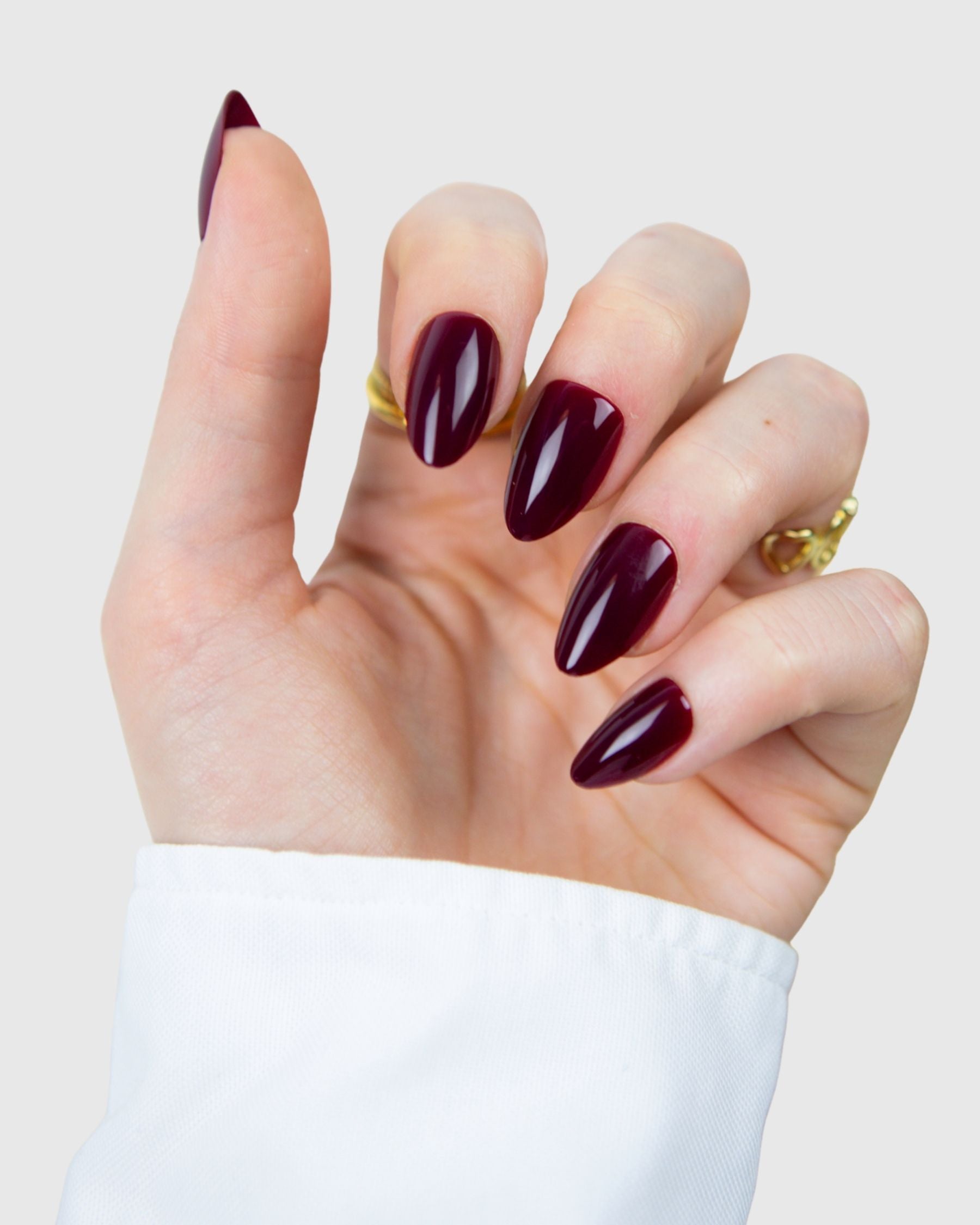 A hand wearing Loste false nails with  burgundy almond design