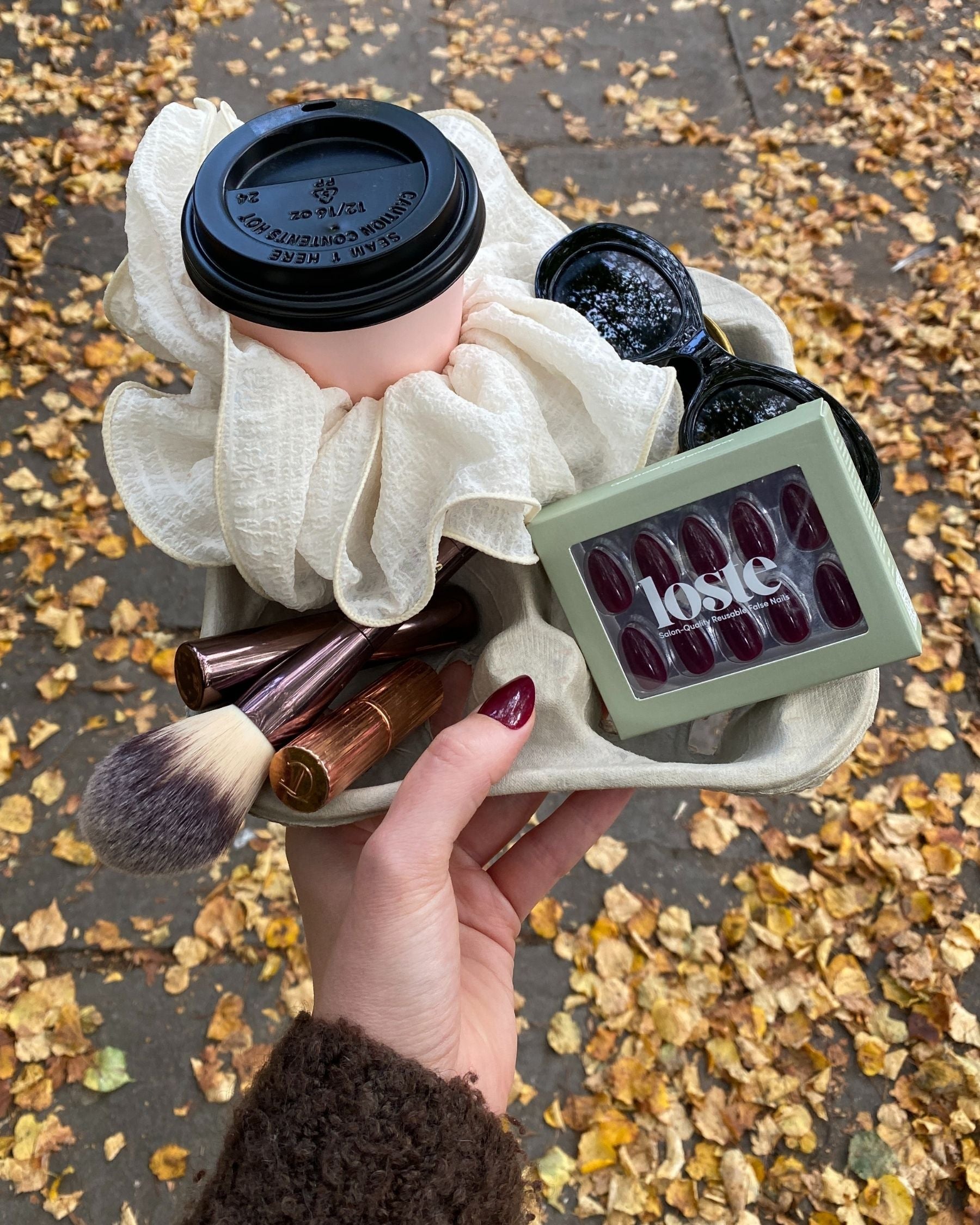 A coffee cup holder flatlay with beauty products, a coffee cup and a box of Loste press-on nails 