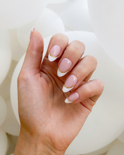 A hand wearing a set of Loste press-on nails with a white and gold French tip design