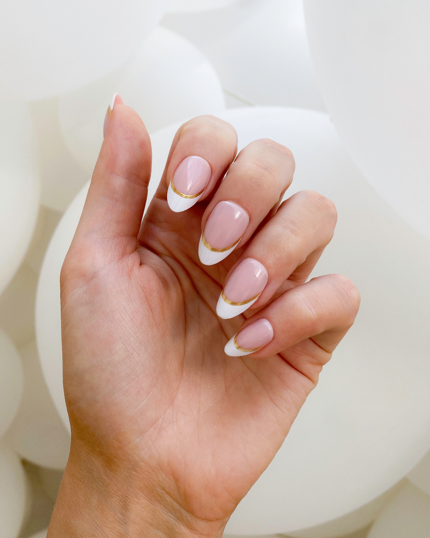 A hand wearing a set of Loste press-on nails with a white and gold French tip design