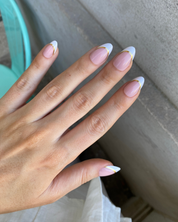 A hand holding a box of Loste press-on nails with a white and gold French tip design