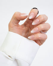 A hand wearing loste press-on nails. The nails have a glossy nude-pink gradient transitioning from a sheer pale pink at the tips to a warmer nude at the base.