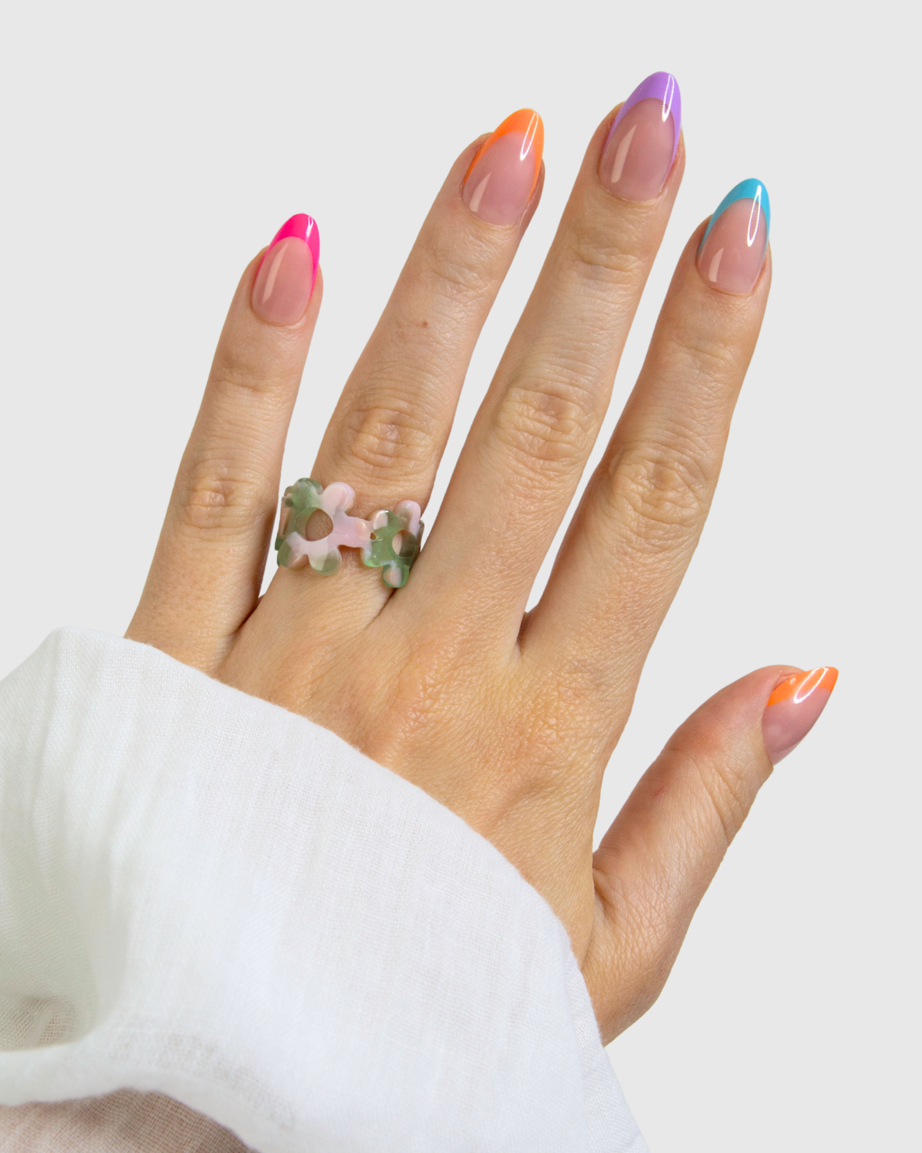 A hand wearing a set of Loste false nails with a multi-colour French design