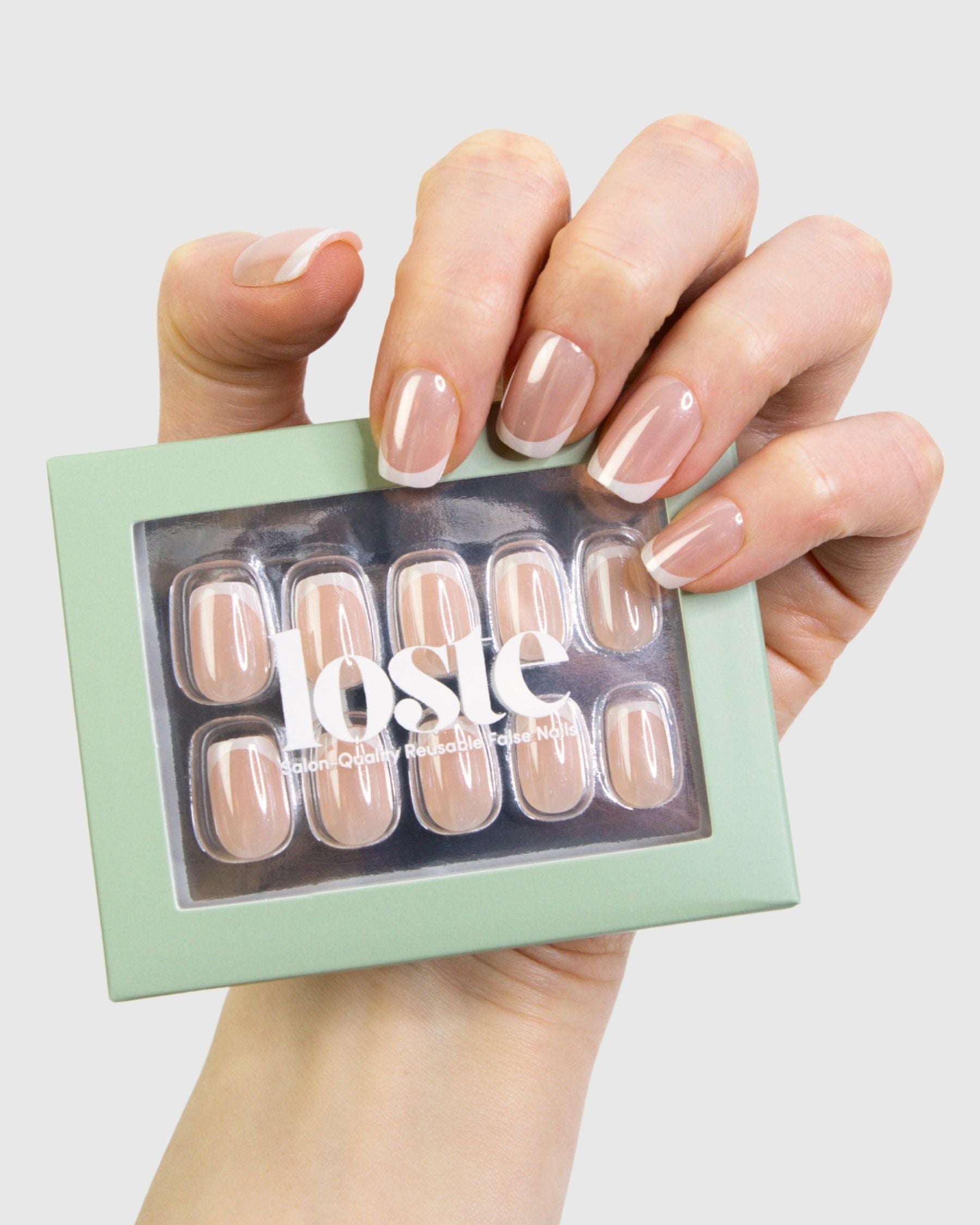 A hand holding a mint green box of Loste false press-on nails. The nails are a sheer nude beige colour with a French tip design.