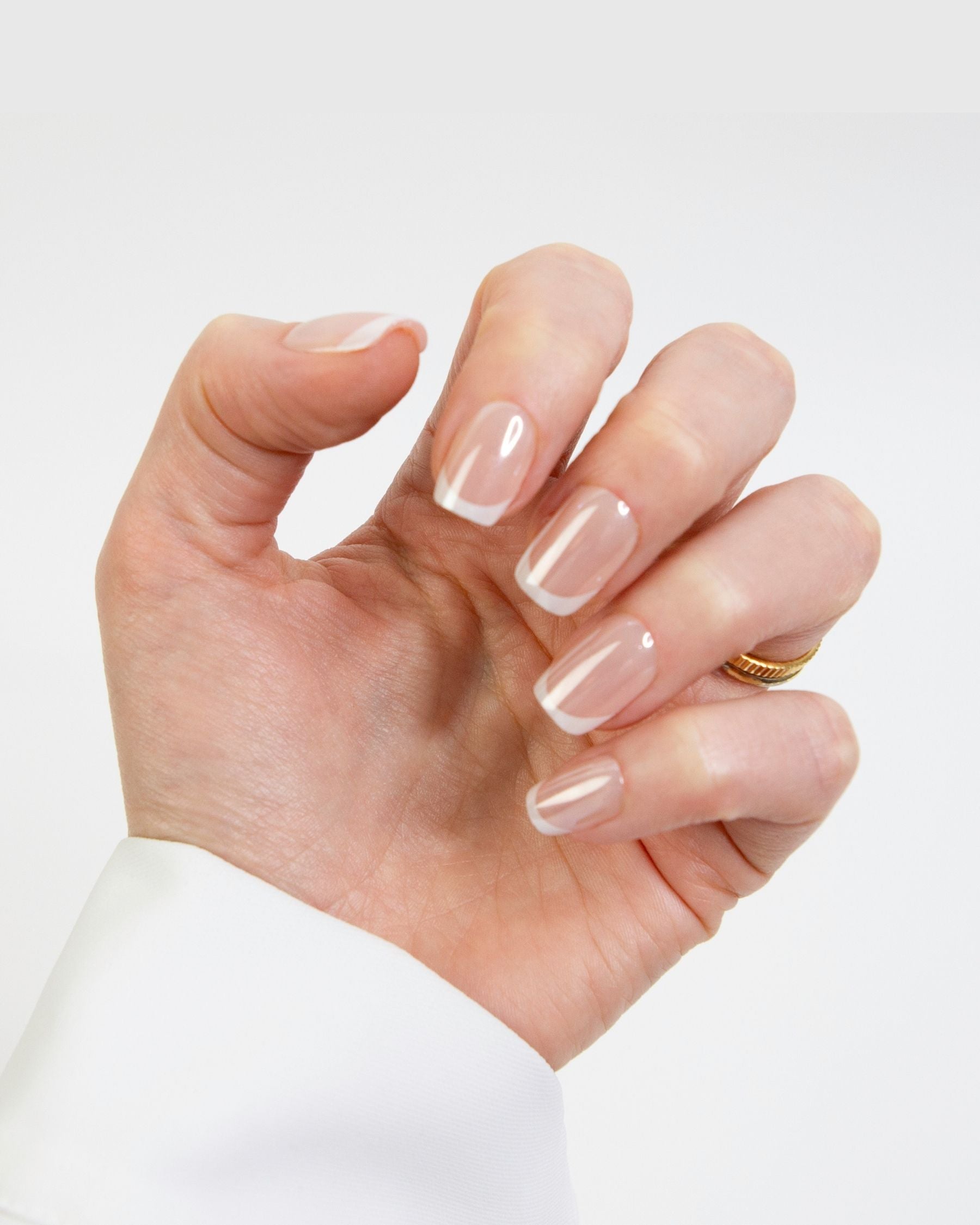 A hand holding wearing Loste false press-on nails. The nails are a sheer nude beige colour with a French tip design.