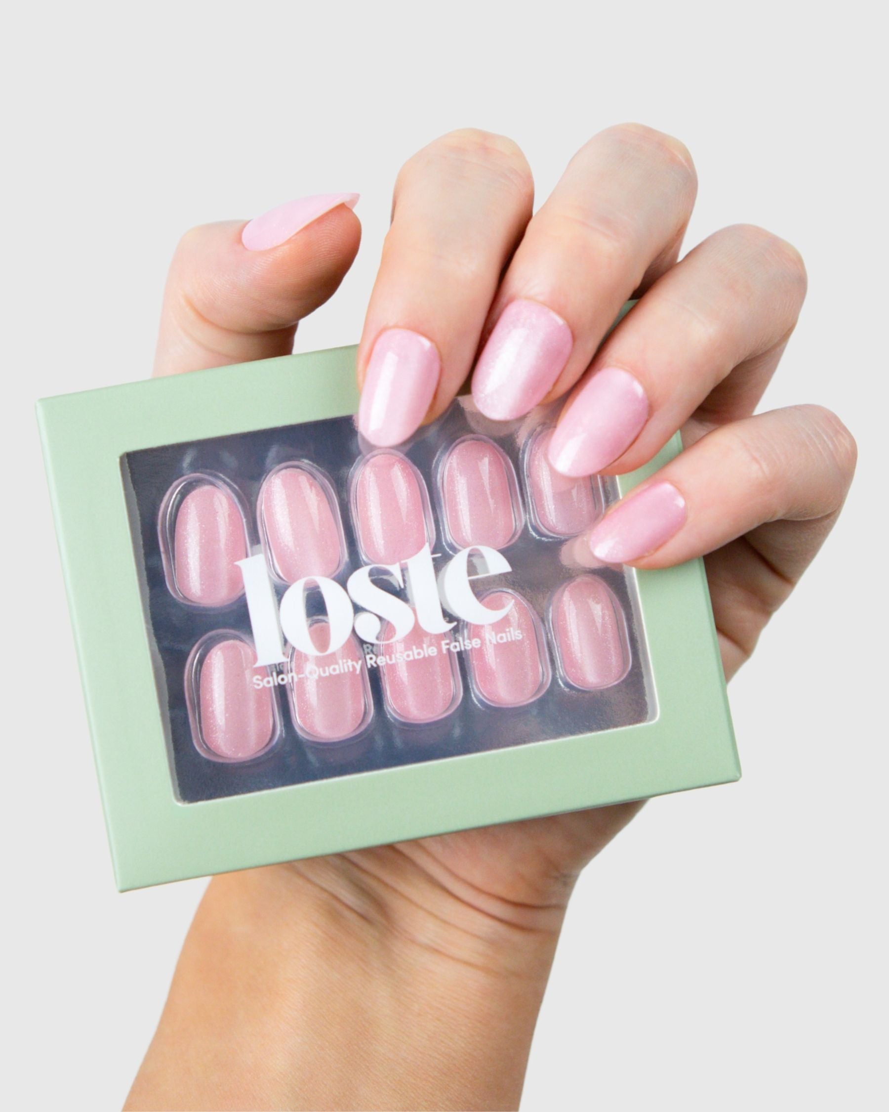 A hand holding a box of Loste press-on nails in a pink cat-eye design